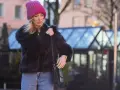 Krótkie futerko stylizacje: blondynka w różowej czapce i czarnym futerku, z jeansami i torebką.