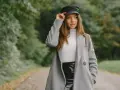 Elegancka kobieta w czapce i szarym płaszczu, prezentująca stylowe stylizacje z szarym płaszczem na tle jesiennego parku.