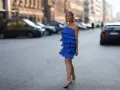 Uśmiechnięta blondynka w zwiewnej, chabrowej sukience z falbankami i złotych sandałkach. Idealne buty do chabrowej sukienki na letni wieczór.
