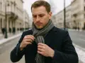 Mężczyzna w granatowym płaszczu poprawia szary szalik. Pokazujemy, jak wiazac szalik meski, by wyglądać stylowo.