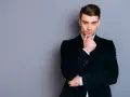 Elegancki mężczyzna w ciemnej, **marynarce aksamitnej męskiej**, z dłonią na podbródku, spogląda wprost.