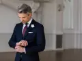 Elegancki mężczyzna w granatowym garniturze i bordowym krawacie poprawia mankiet.
