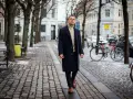 Elegancki mężczyzna w granatowym płaszczu damskim i golfie spaceruje po brukowanej ulicy. Stylowe granatowy płaszcz damski stylizacje.