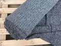 Szary, zwinięty materiał, który jest sztucznym zamiennikiem naturalnej wełny, leży na drewnianej palecie.