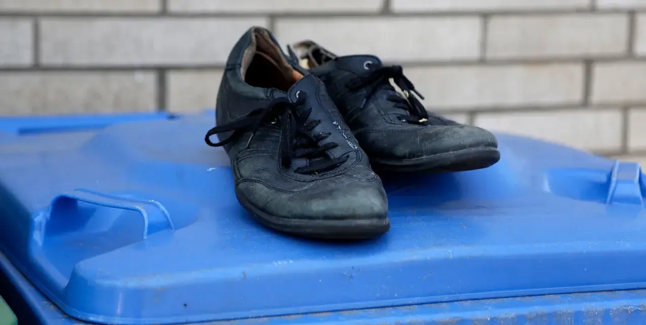 Stare czarne buty na niebieskim koszu na śmieci. Zastanawiasz się, gdzie wyrzucić buty gumowe? To nie są gumowe, ale też już zużyte.