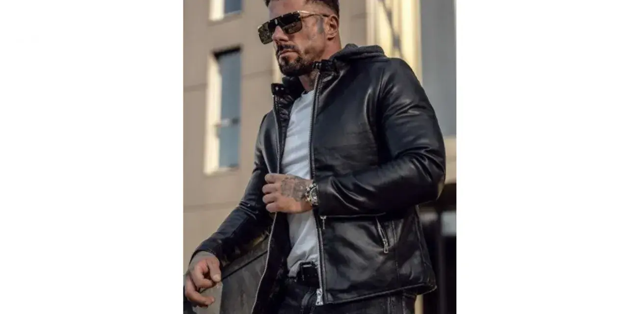Mężczyzna w stylowej, czarnej kurtce woskowanej męskiej, z kapturem, okularach przeciwsłonecznych i tatuażami.