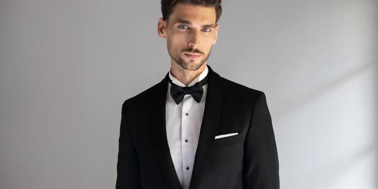 Elegancki mężczyzna w czarnym smokingu z białą poszetką. Dowiedz się, jak dobrać poszetkę do stylizacji.