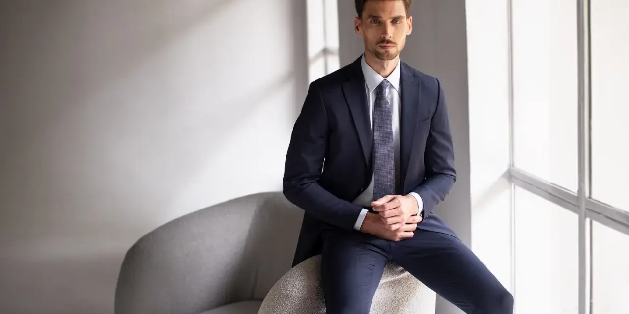 Elegancki mężczyzna w granatowym garniturze i krawacie. Idealny przykład, jak ubrać się na rozmowę kwalifikacyjną mężczyzna, by zrobić dobre wrażenie.