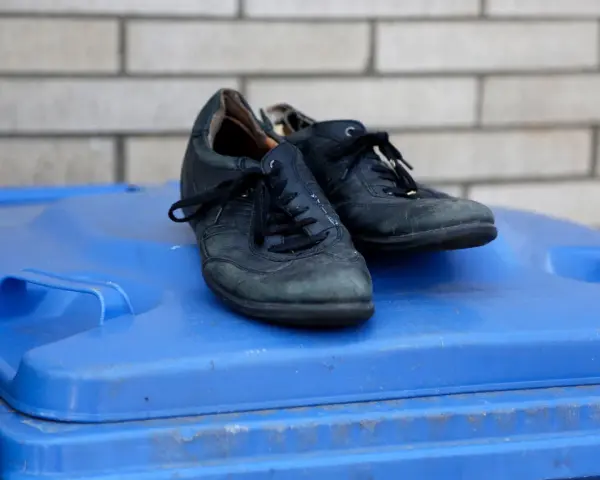 Stare czarne buty na niebieskim koszu na śmieci. Zastanawiasz się, gdzie wyrzucić buty gumowe? To nie są gumowe, ale też już zużyte.