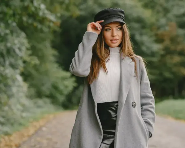 Elegancka kobieta w czapce i szarym płaszczu, prezentująca stylowe stylizacje z szarym płaszczem na tle jesiennego parku.