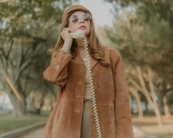 Kobieta w brązowej zamszowej kurtce damskiej rozmawia przez telefon w stylu retro.