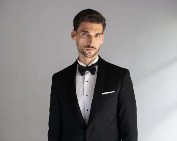 Elegancki mężczyzna w czarnym smokingu z białą poszetką. Dowiedz się, jak dobrać poszetkę do stylizacji.