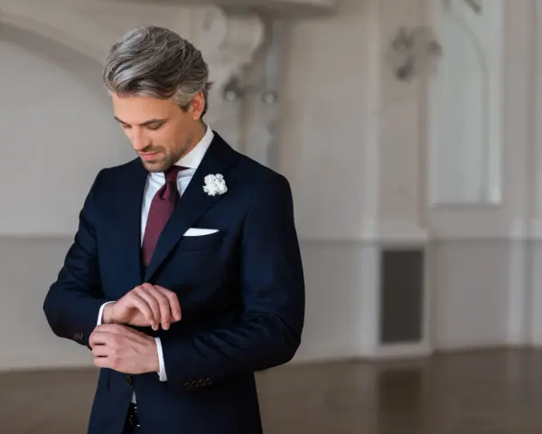 Elegancki mężczyzna w granatowym garniturze i bordowym krawacie poprawia mankiet.