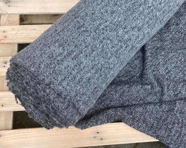 Szary, zwinięty materiał, który jest sztucznym zamiennikiem naturalnej wełny, leży na drewnianej palecie.