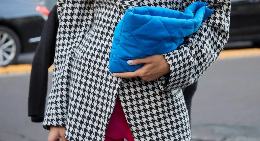 Modna marynarka w pepitkę i jaskrawe spodnie tworzą odważną stylizację. Błękitna kopertówka dodaje koloru.
