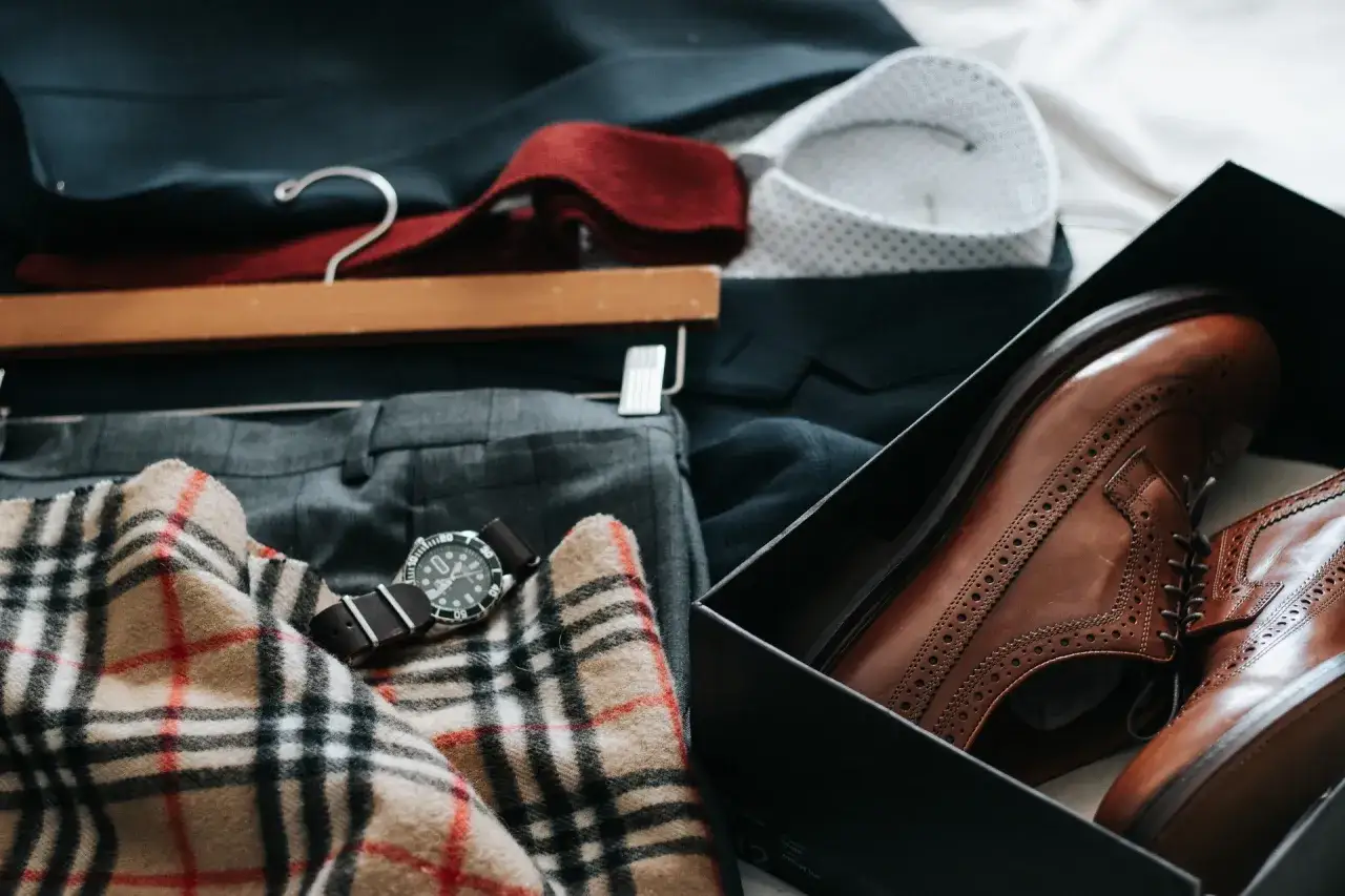 Elegancki zestaw ubrań: garnitur, koszula, krawat, szalik w kratę, zegarek i nowe, brązowe buty. To kwintesencja włoskiego stylu męskiego.