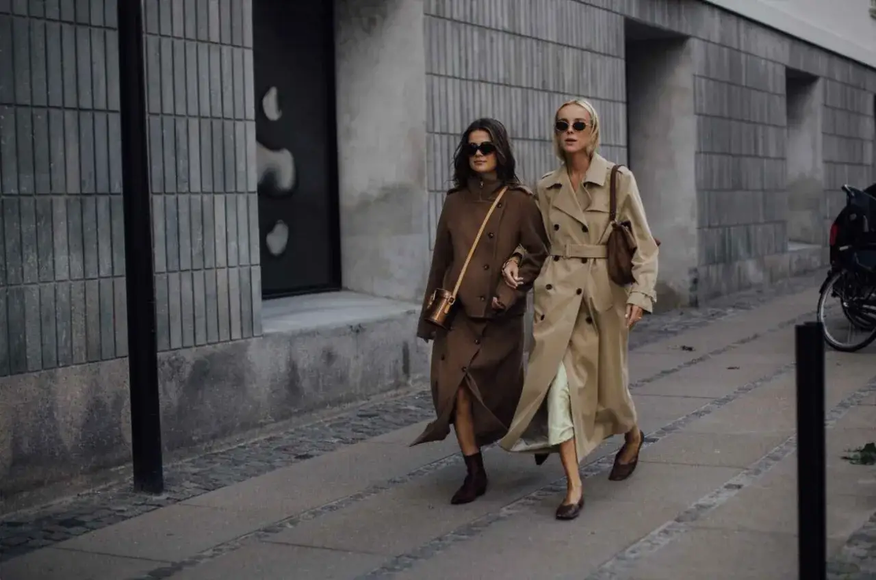 Dwie kobiety w eleganckich płaszczach, uosobienie stylu duńskiej marki odzieżowej, spacerują ulicą.