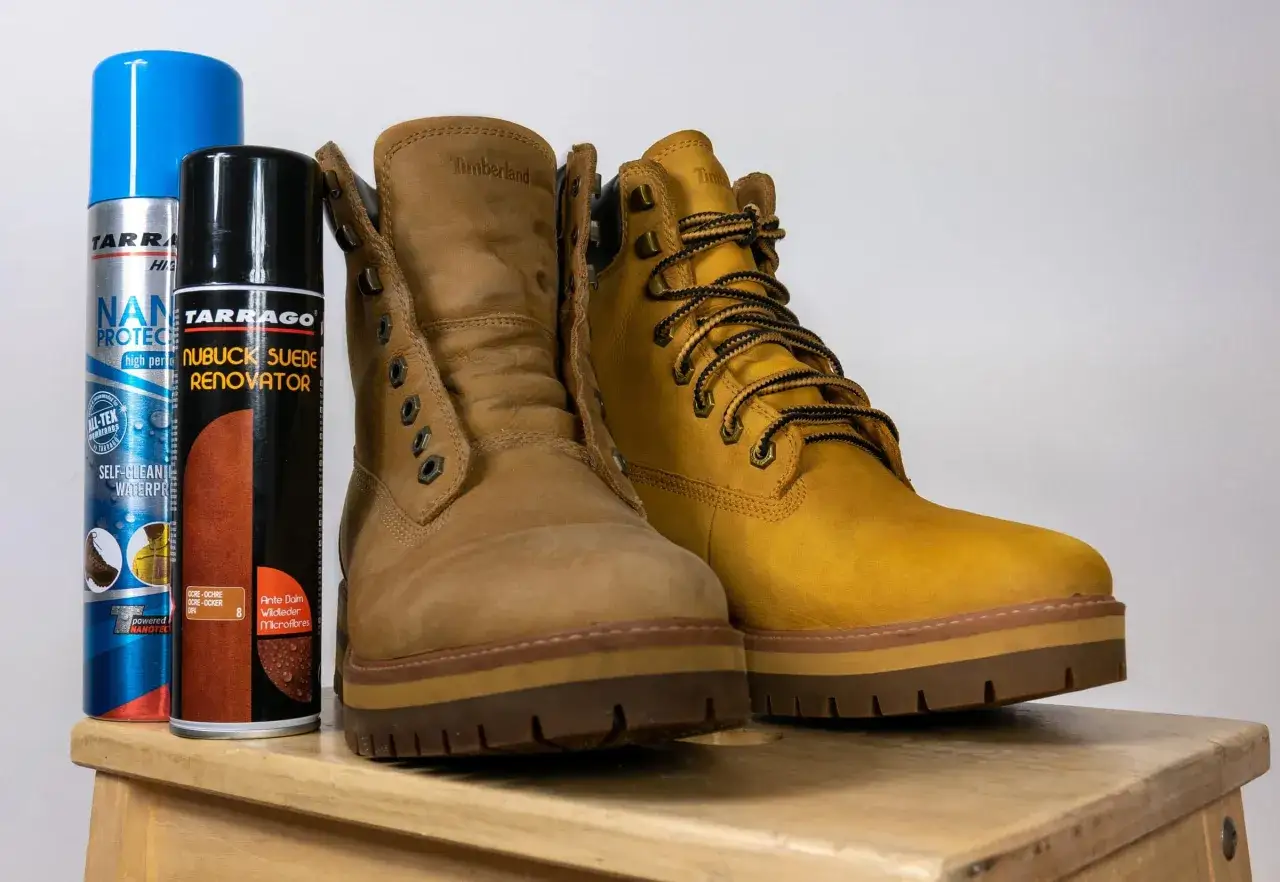 Dwa buty Timberland, jeden jaśniejszy, drugi ciemniejszy, obok preparatów do farbowania butów zamszowych.
