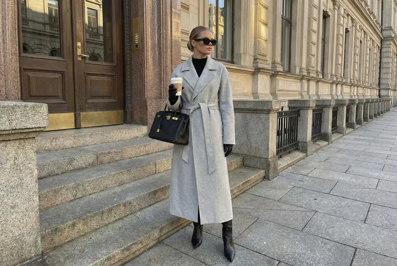 Elegancka kobieta w szarym płaszczu, czarnych rękawiczkach i butach, z torebką i kawą na wynos, prezentuje stylowe stylizacje z szarym płaszczem.