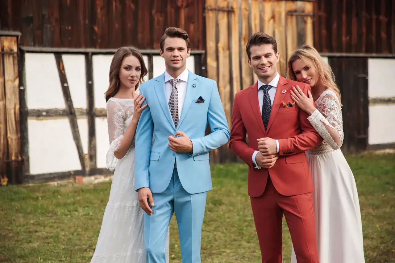 Eleganccy panowie w błękitnym i rudym garniturze, obok nich panie w białych sukniach. Inspiracja, jak się ubrać na wesele jako gość.